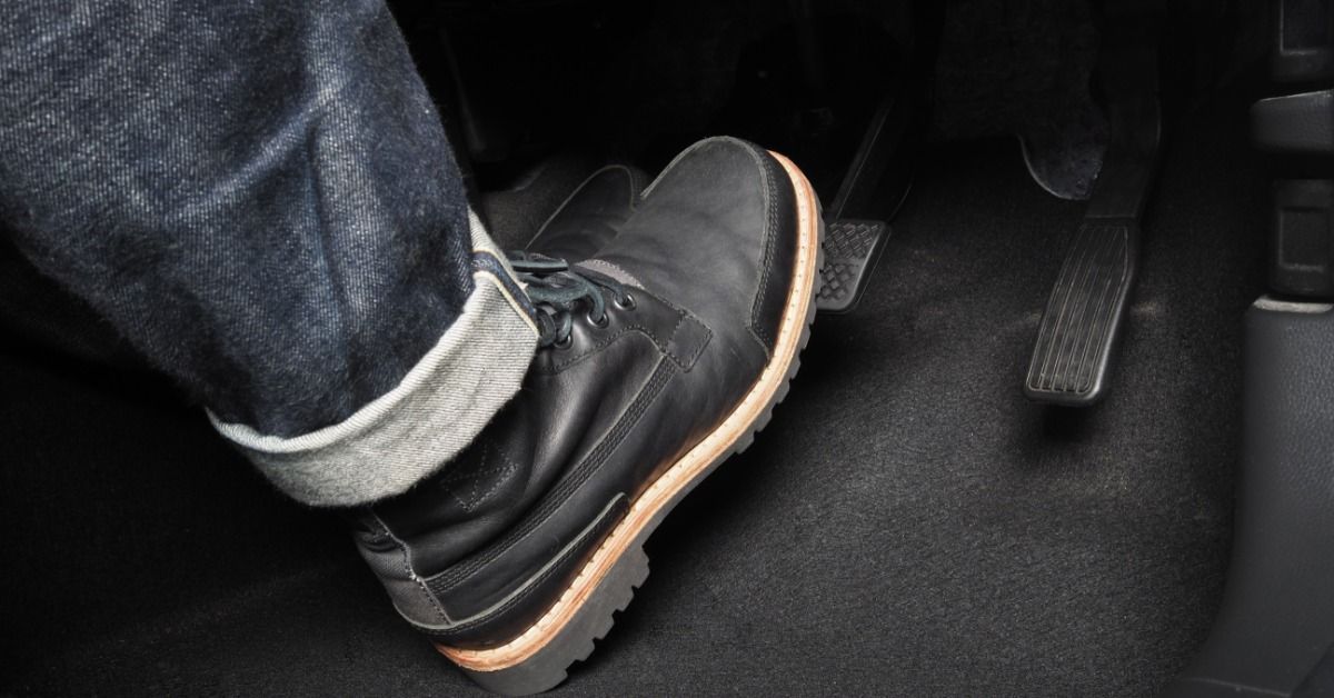 A person driving a car is wearing jeans and black boots while applying one foot on the brakes in their vehicle.
