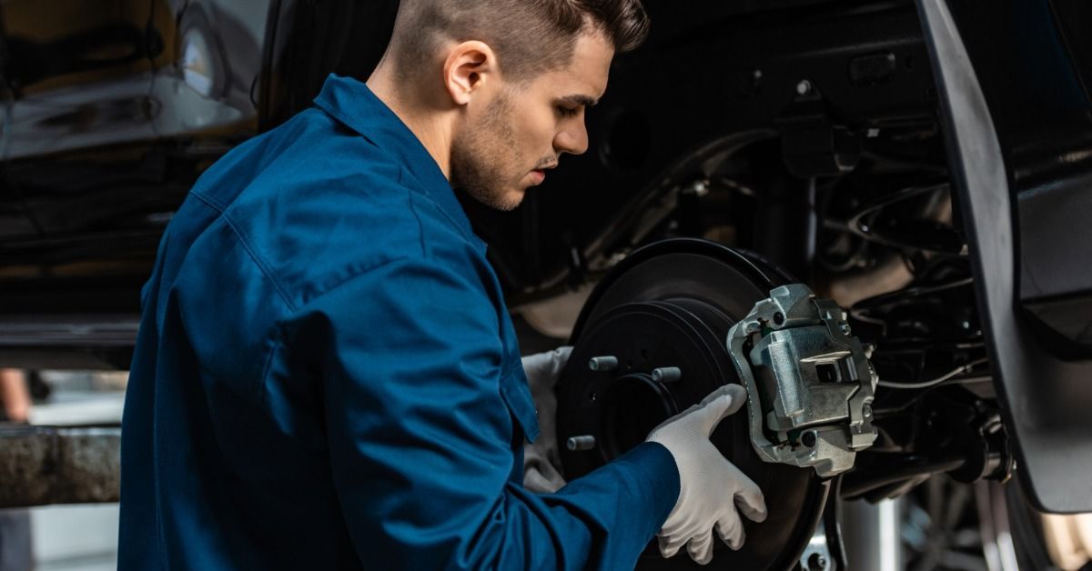 A mechanic wearing a blue uniform with white gloves installs a new brake disk on a car.