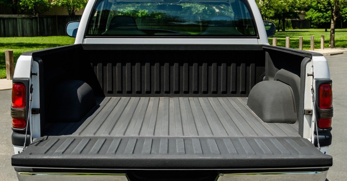 A pickup truck is parked on a residential street on a sunny day with its truck bed open and completely empty.