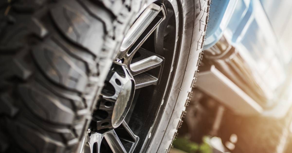 The sun is shining brightly on a blue truck that is parked. The tires have deep treads for off-roading.