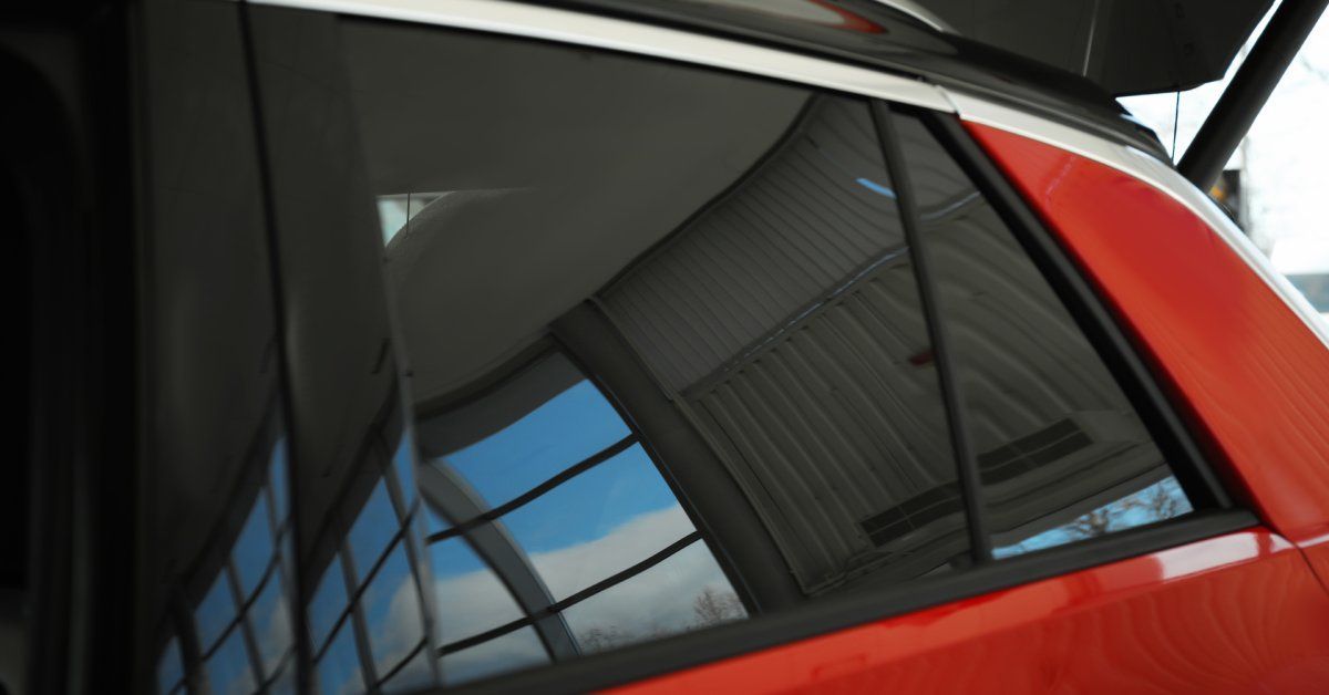A big bright red car with dark tinted windows is parked outside. The car has its trunk door fully open.