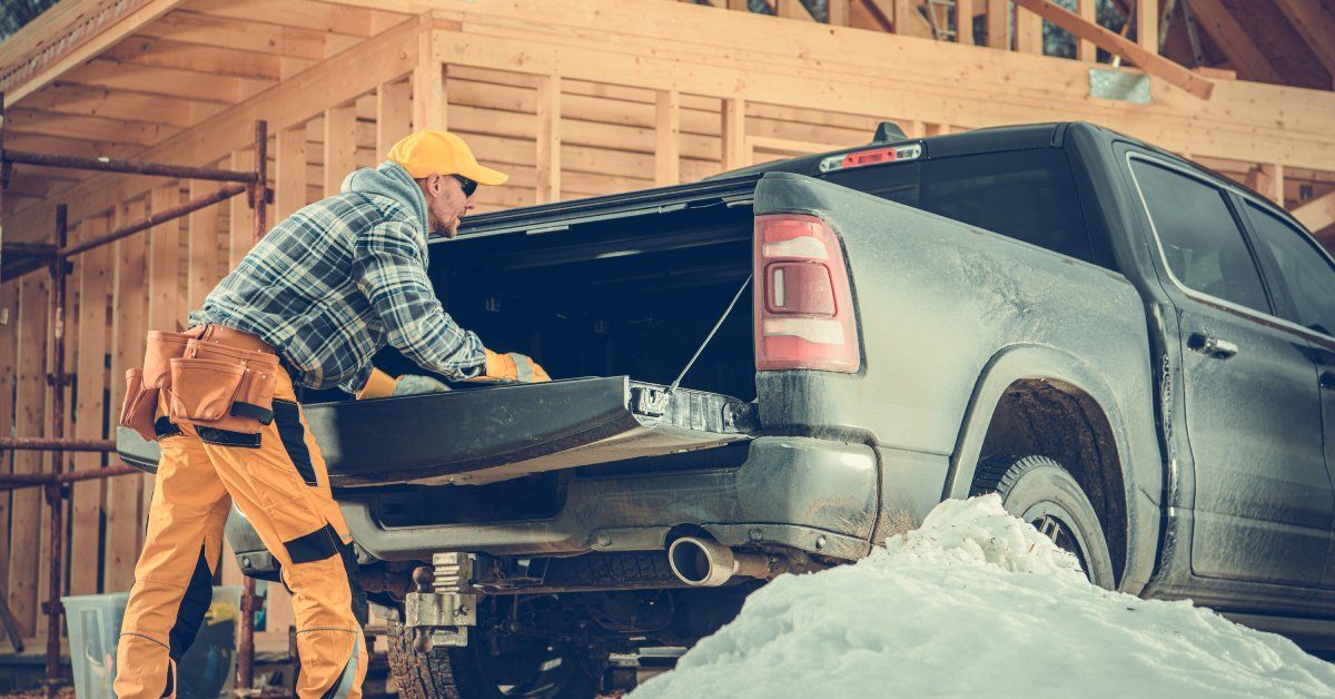 A black pickup truck with its truck bed open next to a construction site. A construction worker is reaching inside.