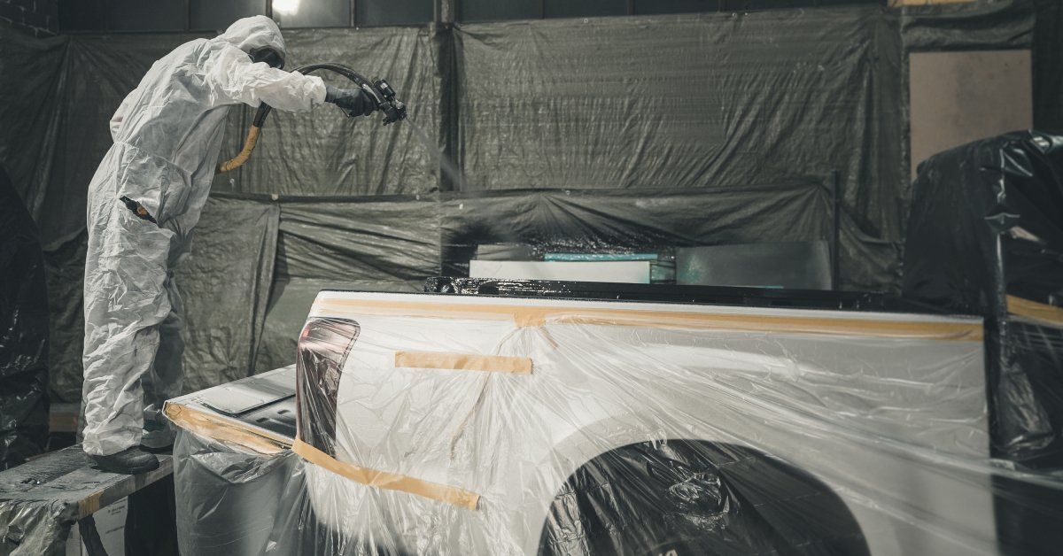 A person spraying a bed liner inside the bed of a pickup truck. The truck is covered in plastic tarps.