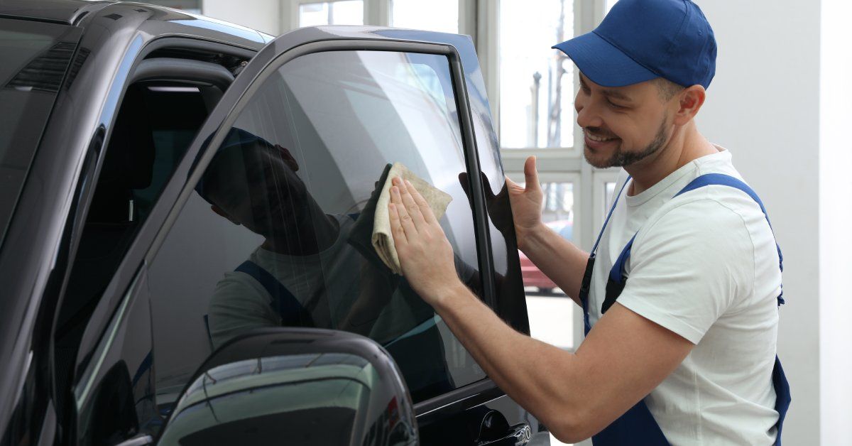 A person wearing a blue hat and blue overalls smiling while wiping a car window.