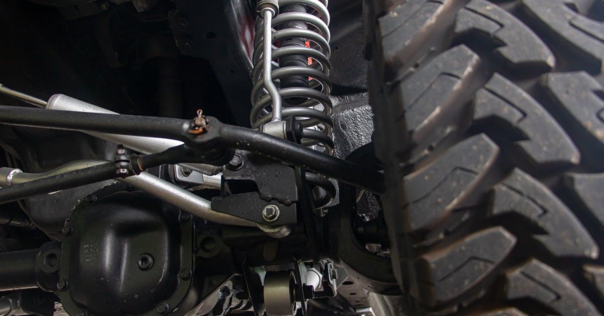 A truck parked near tall green trees outside. The truck has thick off-road tires and a robust suspension system.