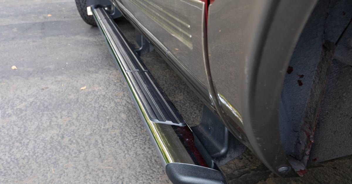A large truck with a long black running board installed near the tires. The car is parked outside on a driveway.
