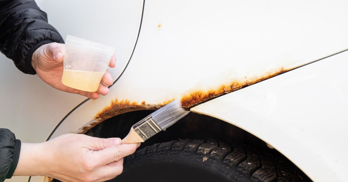 A person using a small paint brush to apply a protective coating to a slim patch of rust on a white truck.