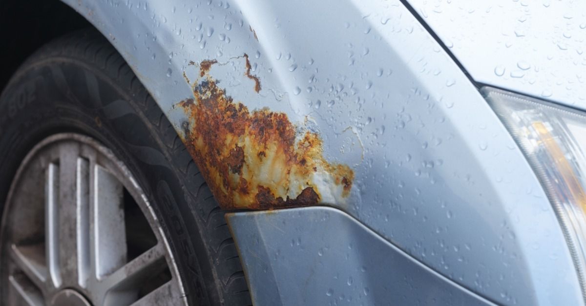 A large patch of rust spreading on the exterior of a light gray truck’s wheel well. The truck is cov