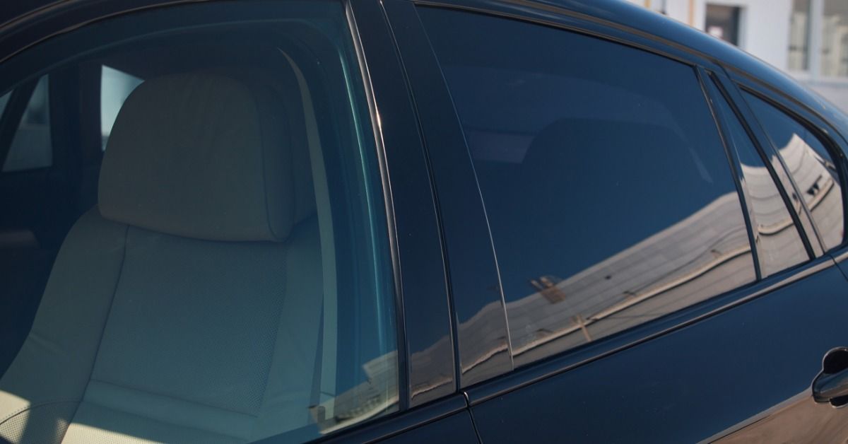 A black car parked in front of a white building during the daytime. Only the rear driver’s side window is tinted.