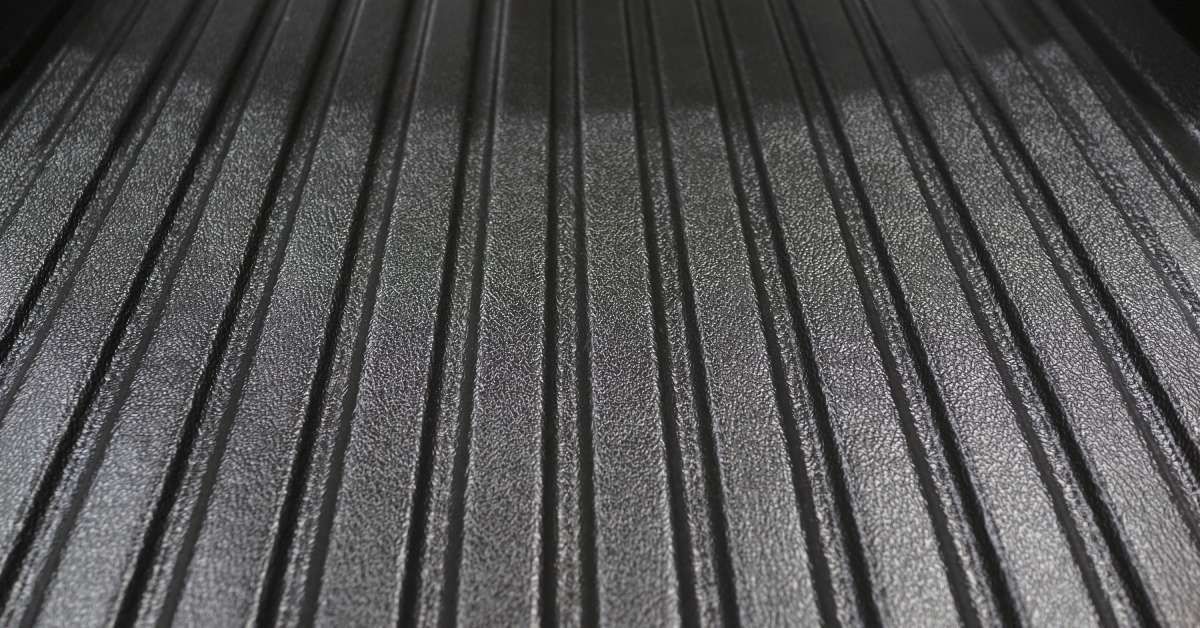 A black pickup truck bed that is empty and clean. There is a bright light shining down on the truck bed from above.