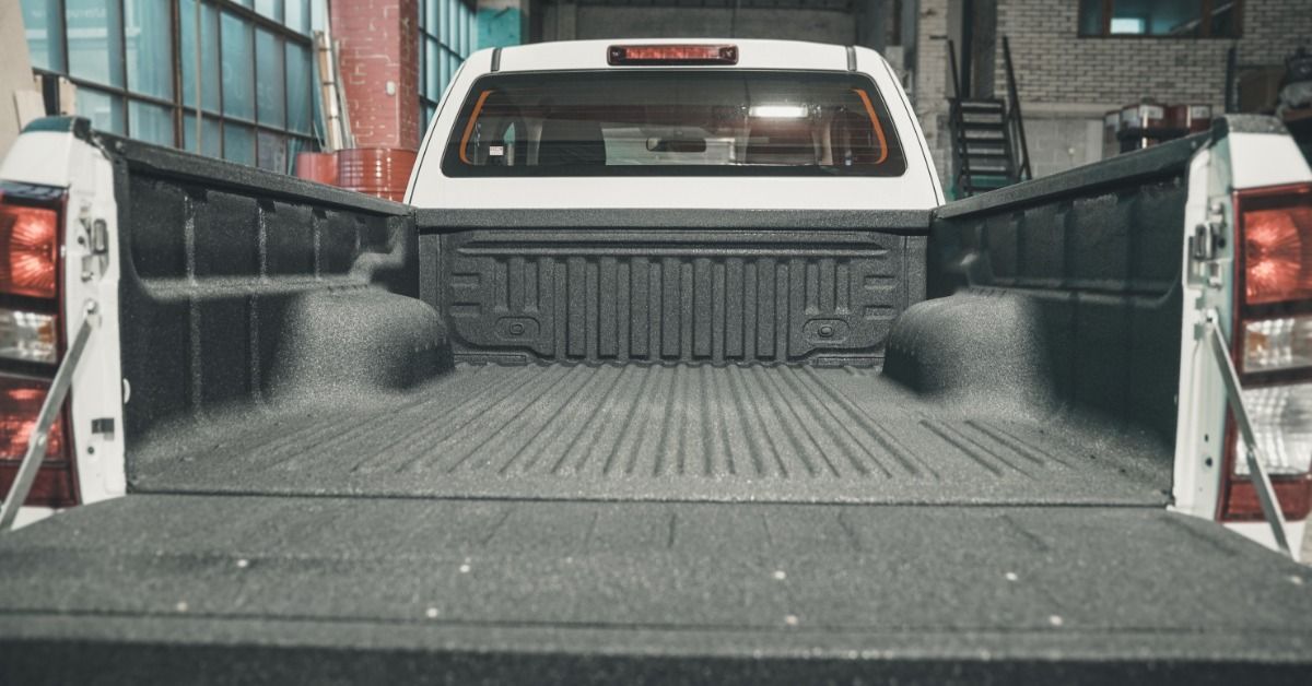 A white truck parked inside a wide garage with large windows. The truck bed door is down.