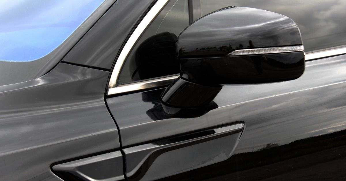 A large black car with dark tinted windows parked outside during the daytime. Minimal sunlight reflects off the car.