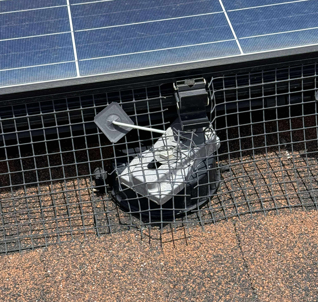Solar panel installer on a rooftop, wearing gloves, orange vest, and blue hat, working on panels in sunlight.