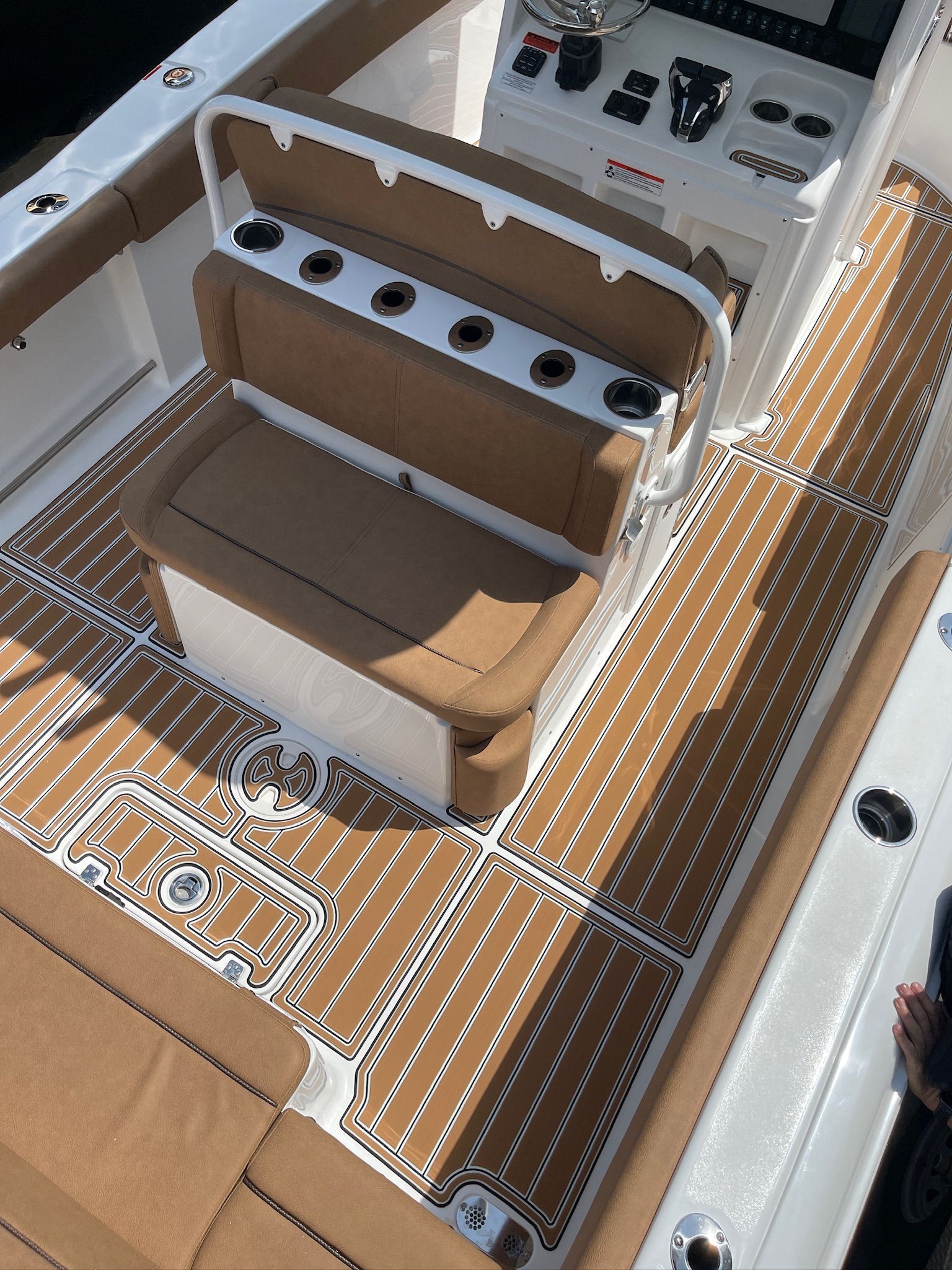 Boat deck with brown and white flooring, a brown seat with cup holders, and a white console.