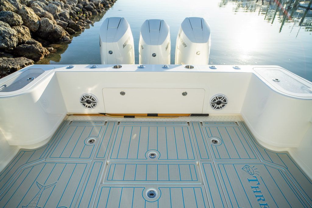Stern of a white boat with three outboard motors, featuring a blue-lined deck and speakers.