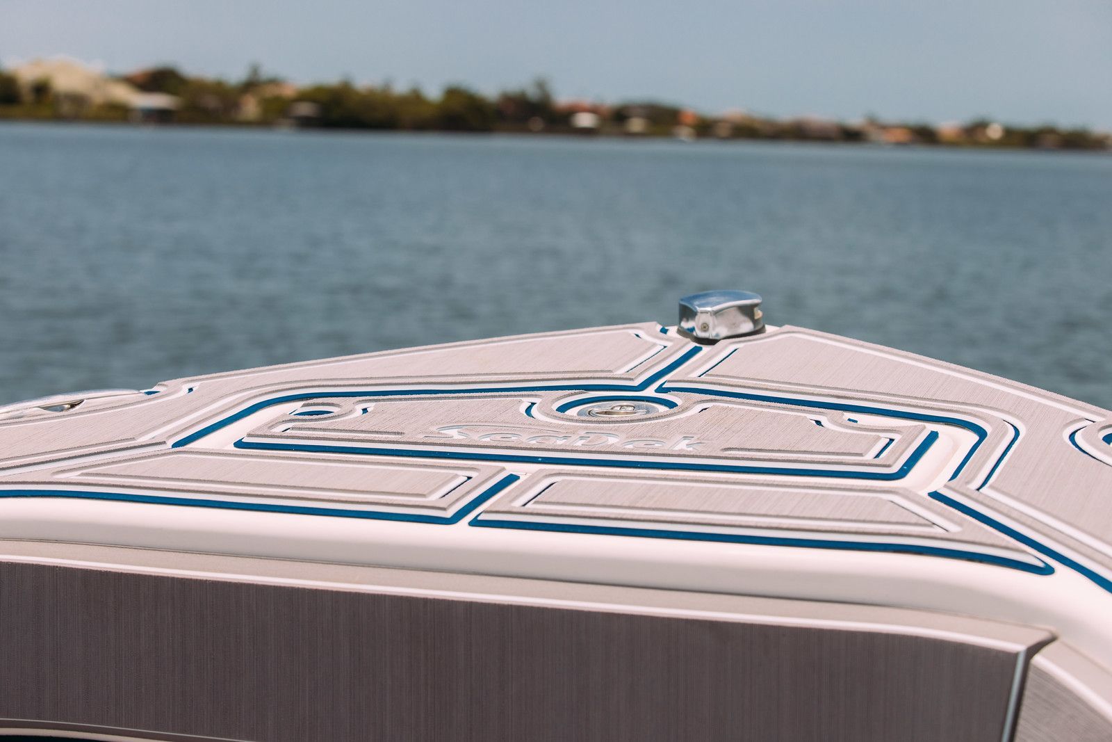 Bow of a boat with gray and blue trim on the water, with blurred land in the background.