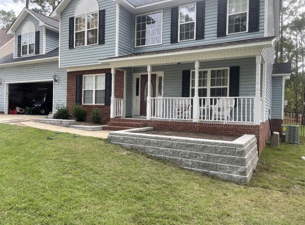 A large house with a large porch and a brick wall in front of it.