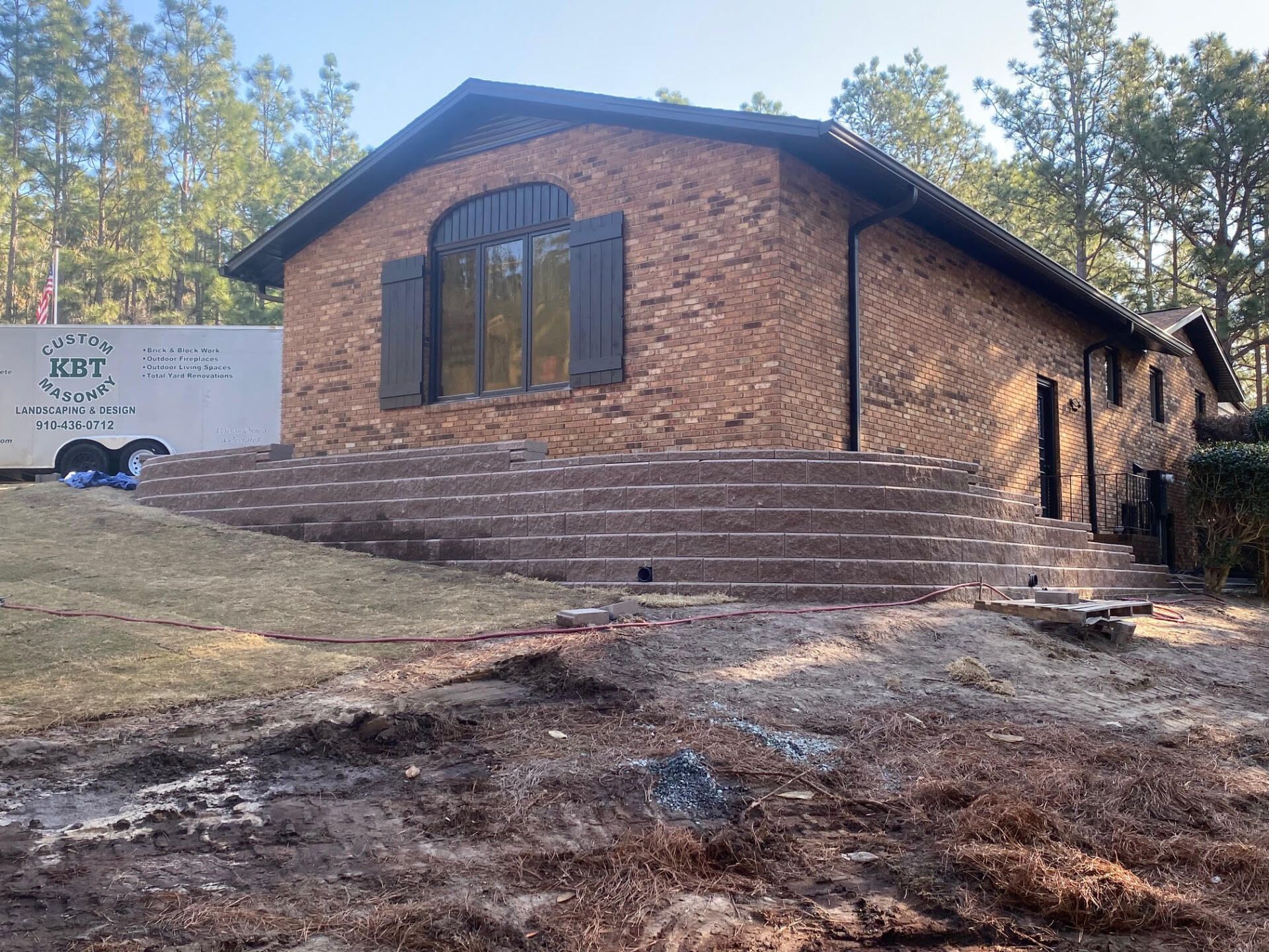 A large brick house with stairs leading up to it is surrounded by trees.