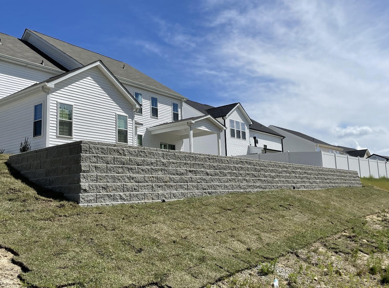 A large white house with a stone wall in front of it.
