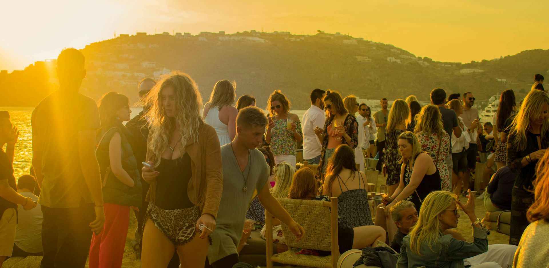 A large group of people are gathered on a beach at sunset.