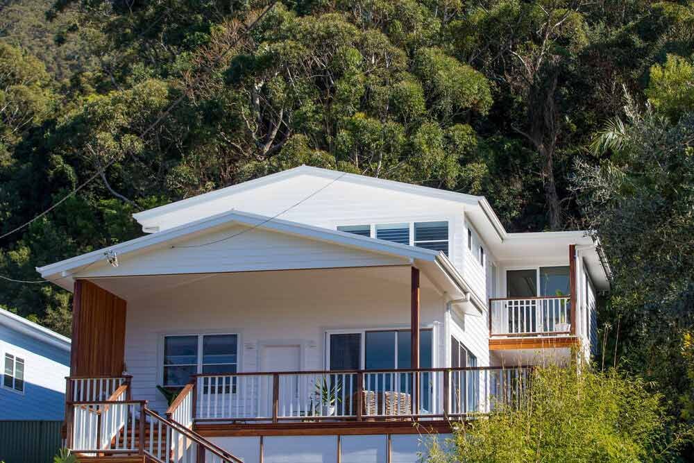 A Large White House With a Balcony is Sitting on Top of a Hill Surrounded by Trees — DeBu Studios In Russell Vale, NSW