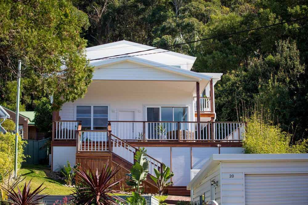 A White House With a Large Deck and Stairs is Surrounded by Trees — DeBu Studios In Russell Vale, NSW