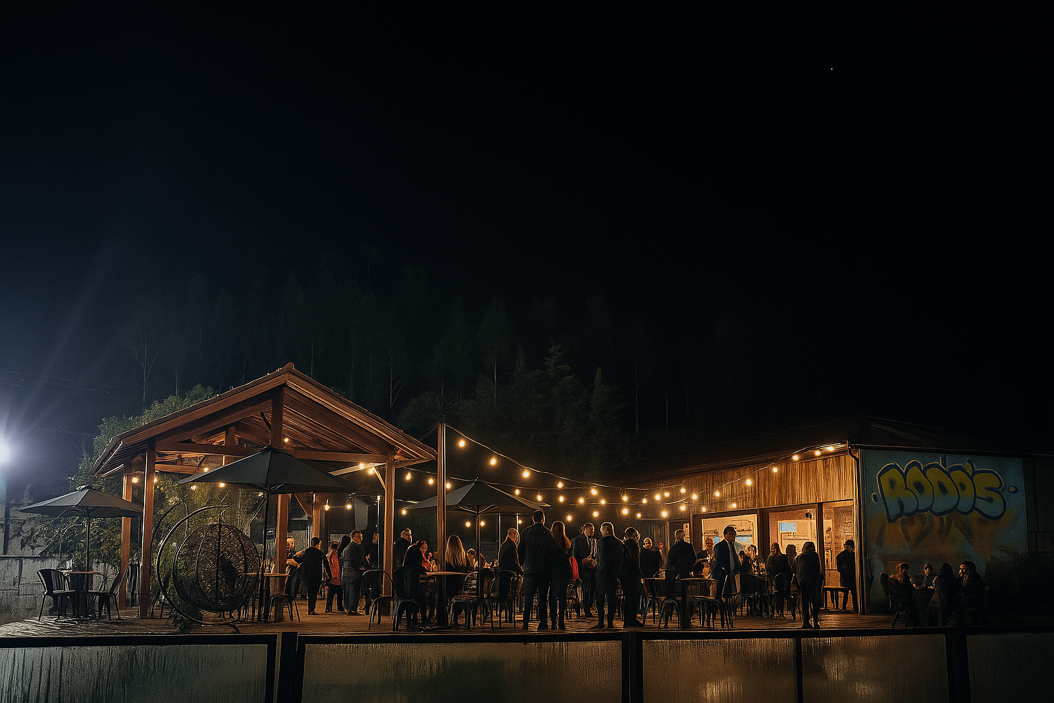 Pavilhão noturno ao ar livre com luzes de corda, uma multidão e um mural colorido à direita.