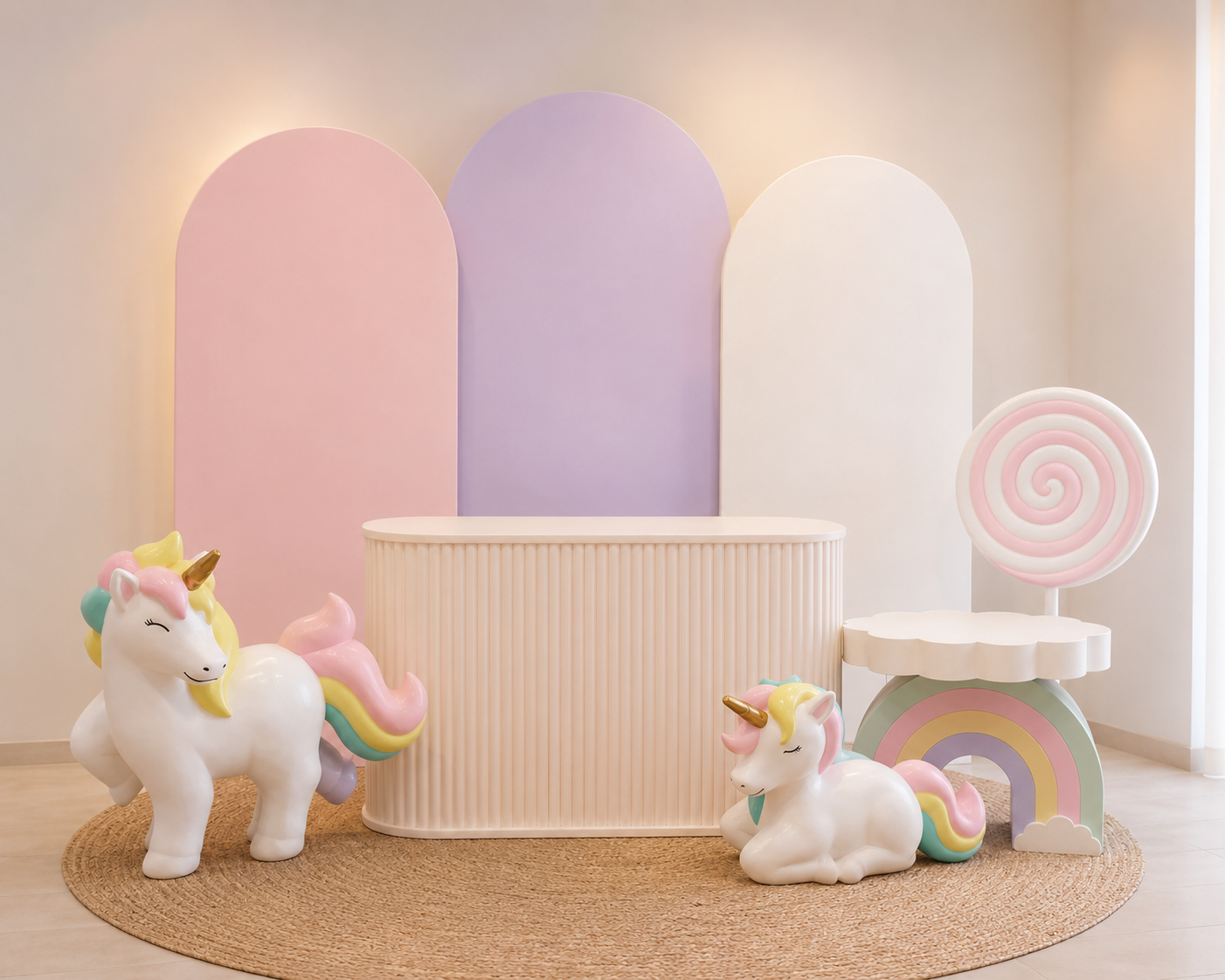 Decoração de unicórnio em tons pastel com detalhes de arco-íris, pirulito e arcos sobre um fundo neutro de mesa.