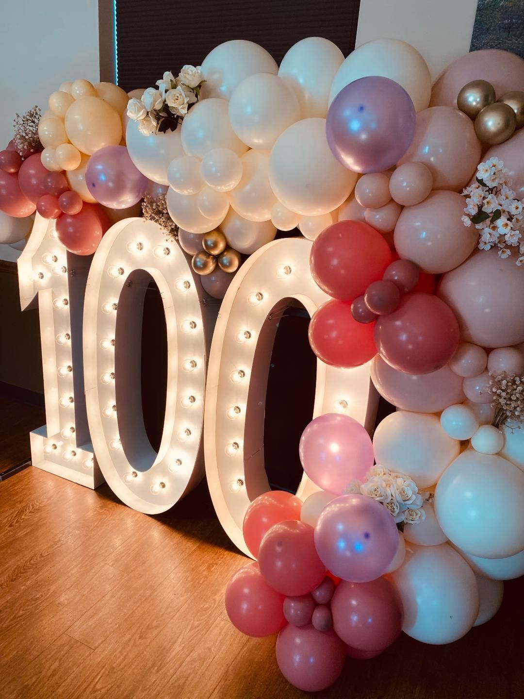 “100” marquee letters surrounded by pastel balloon garland at a birthday-style celebration