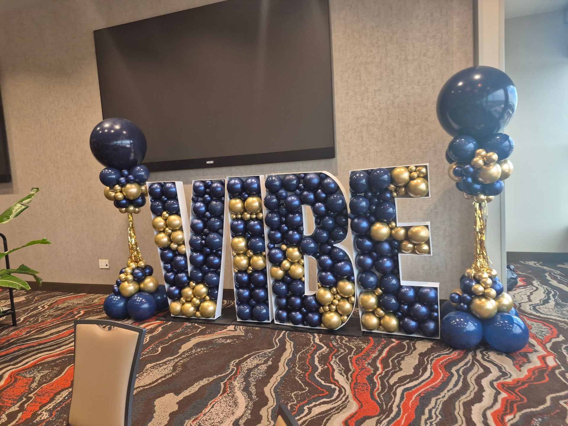 Blue and gold balloon display spelling “JIRE” in a conference room