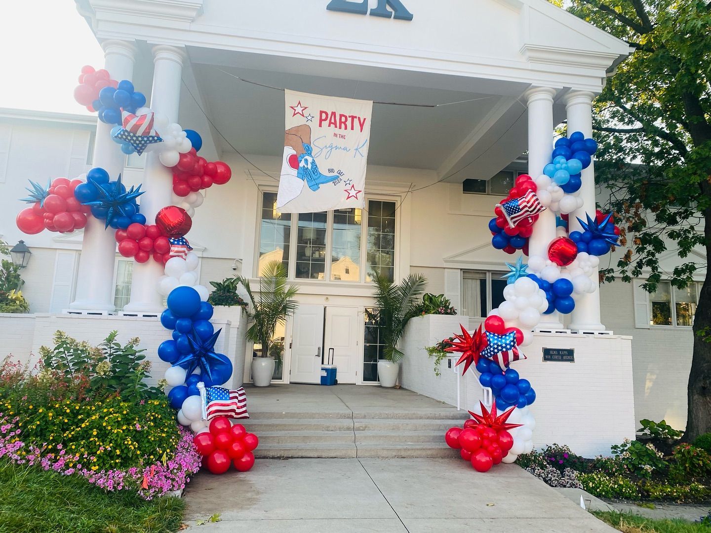 House entrance decorated with red, white, and blue balloon columns and a “Party” sign on the porch