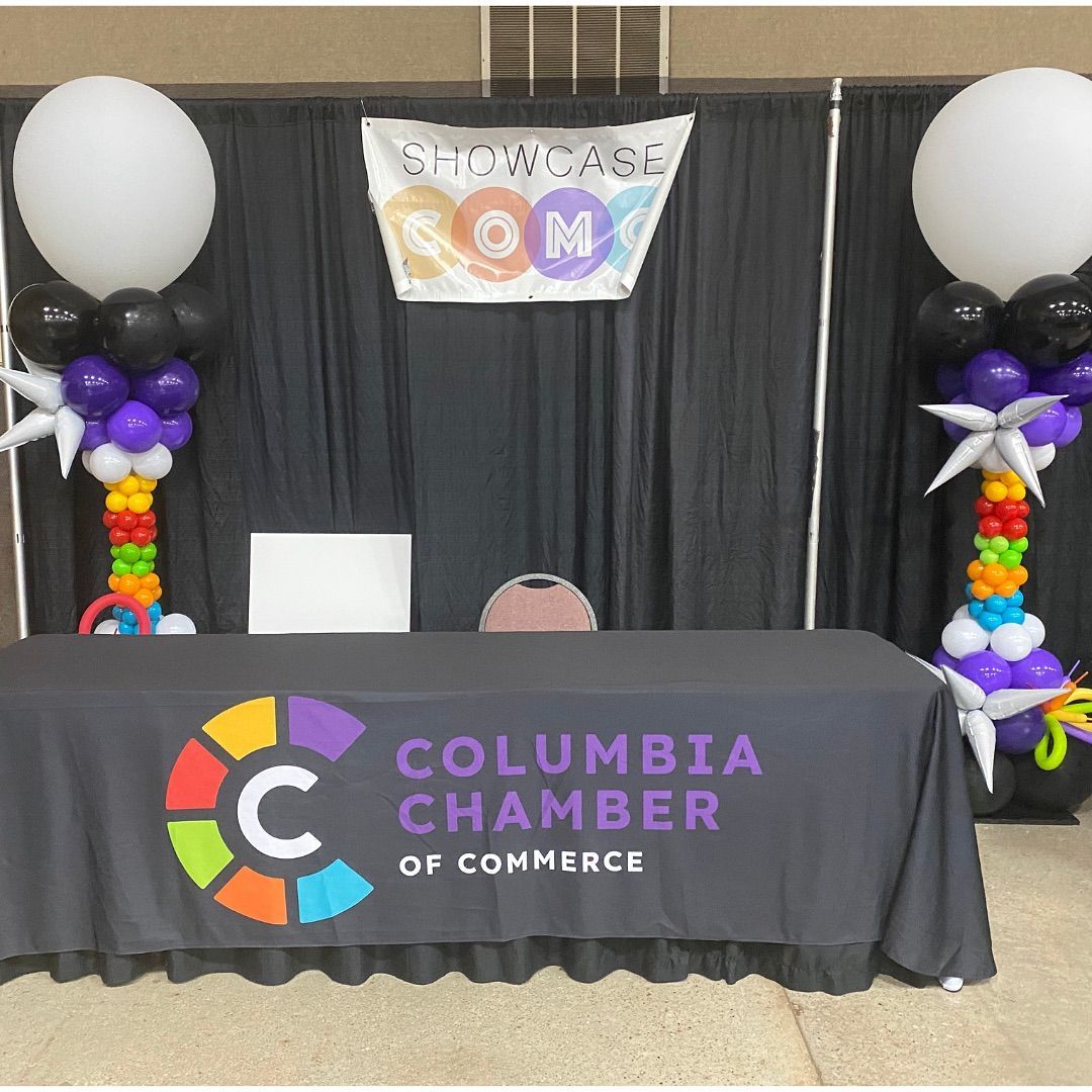 Columbia Chamber of Commerce event booth with balloon columns, black drape backdrop, and table banner