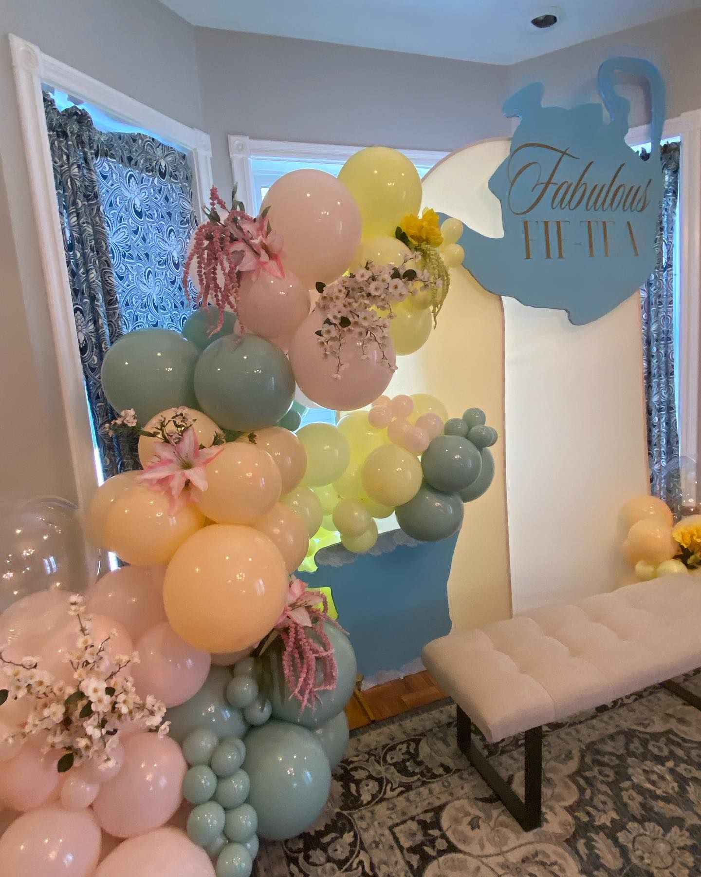 Pastel balloon display and floral decor beside a cushioned bench in a bright entryway
