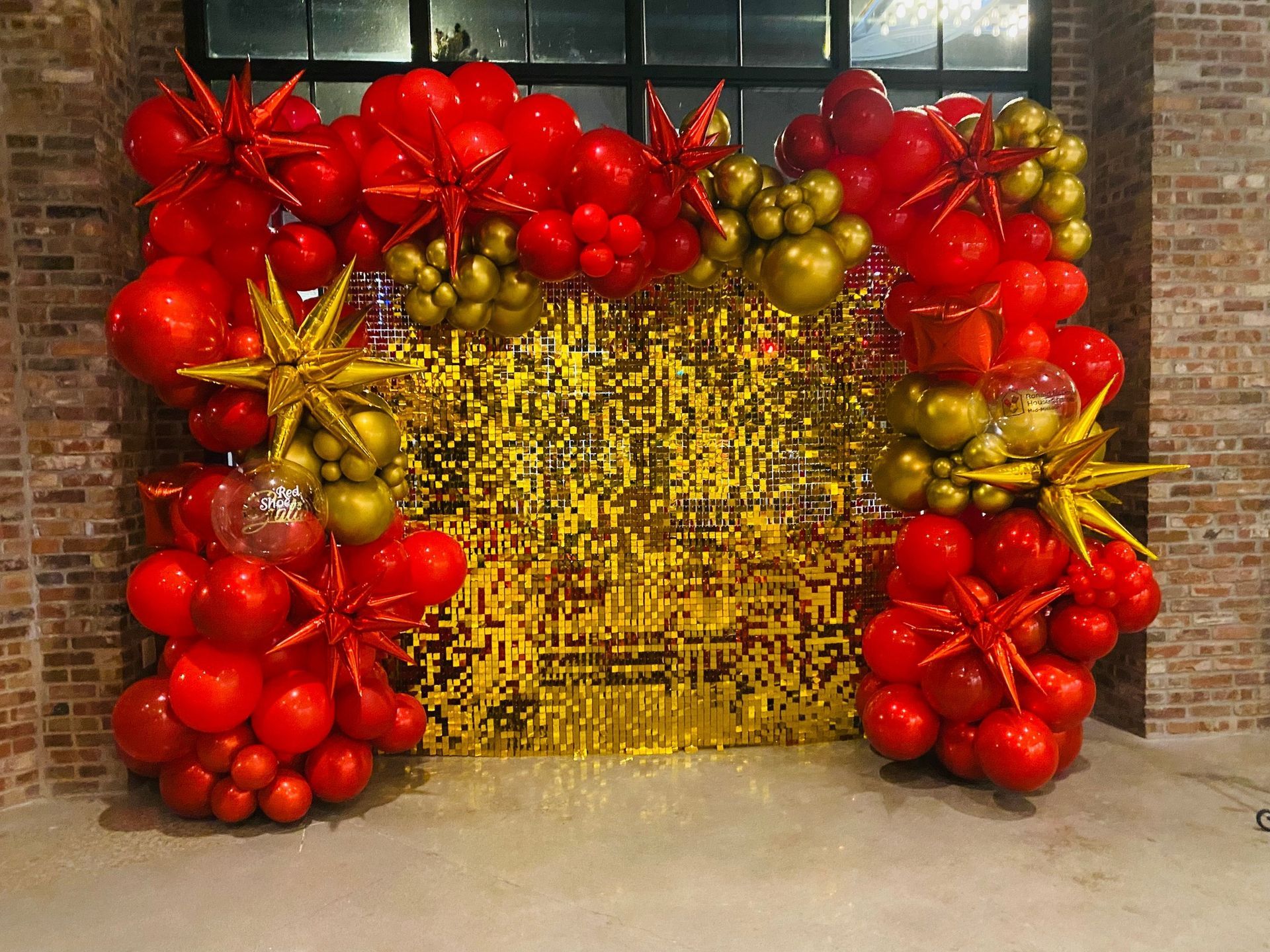 Festive red and gold balloon arch framing a yellow backdrop outside a brick building
