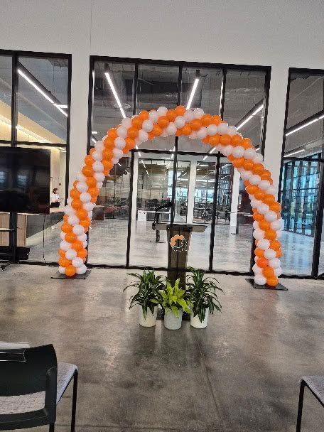 Orange-and-white balloon arch at a building entrance with potted plants in front