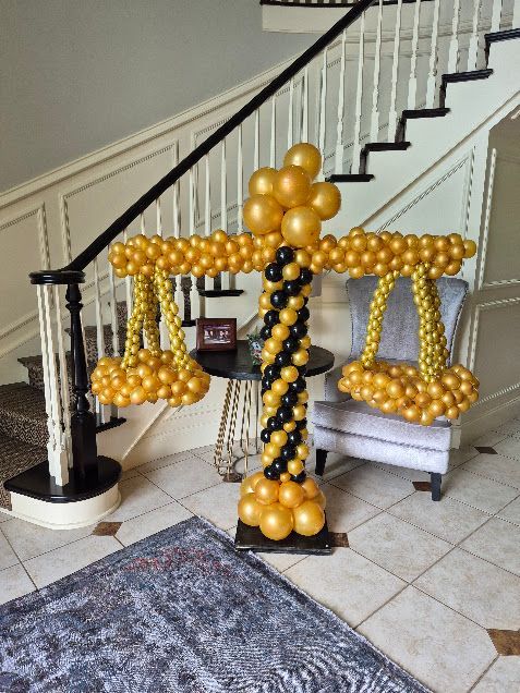 Balloon sculpture of a gold-and-black balance scale in a home stairway.