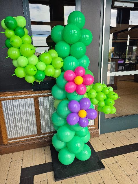 Green balloon sculpture with pink and purple flowers displayed indoors on a black base.