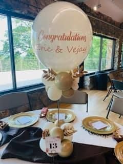 Wedding reception table with a “Congratulations Eric & Vejay” balloon centerpiece and gold accents