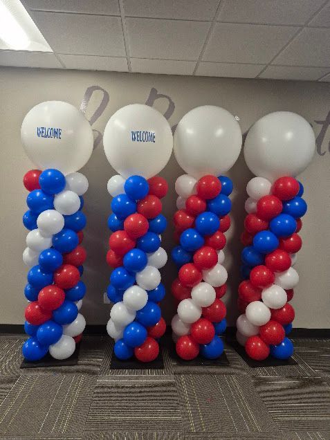 Three balloon columns in red, white, and blue with white balloon tops at an indoor event booth.