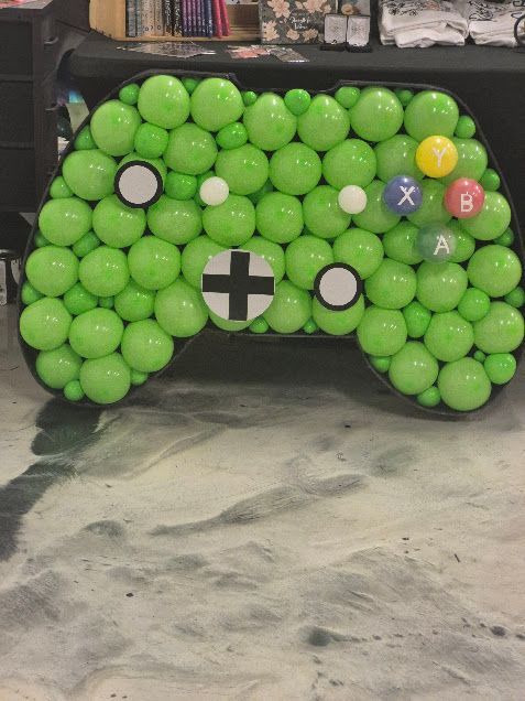 Green balloon-covered Xbox-style game controller prop with colored button symbols on the front.