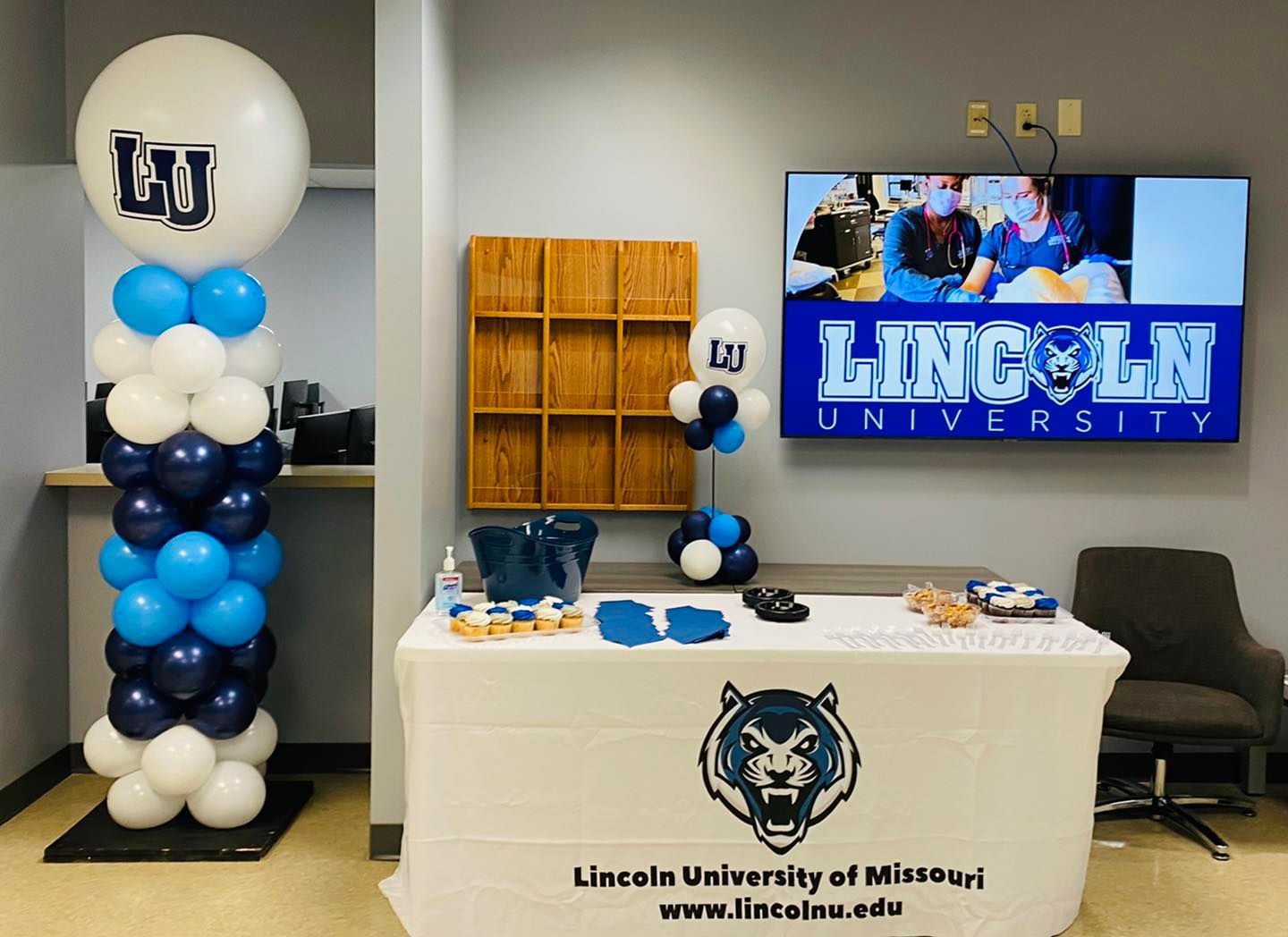 Lincoln University of Missouri event table with blue-and-white balloon display, table banner, and TV screen.