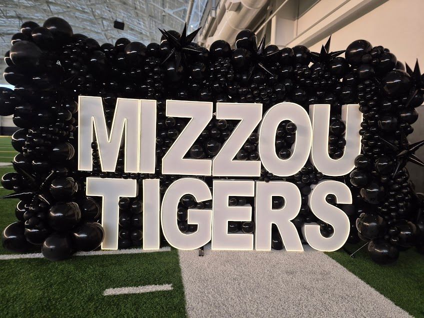 White “MIZZOU TIGERS” letters in front of black balloons on a building walkway