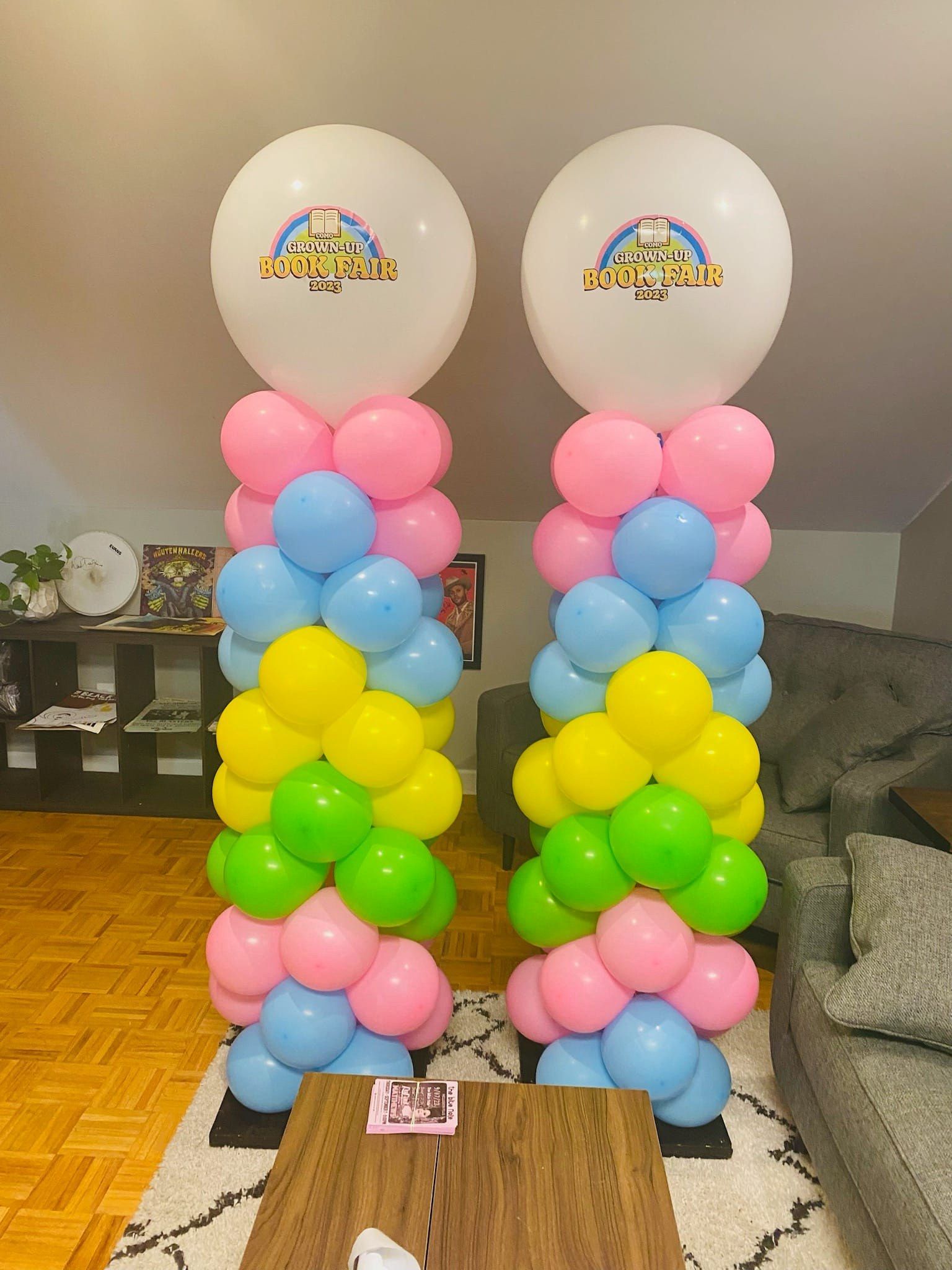 Two pastel balloon towers with white balloons on top and rainbow-colored balloons below in a room