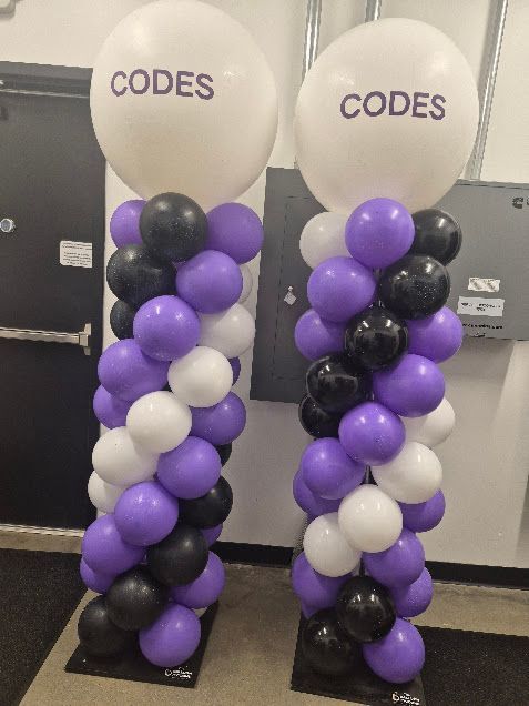 Two purple and black balloon columns with white top balloons labeled “CODES”