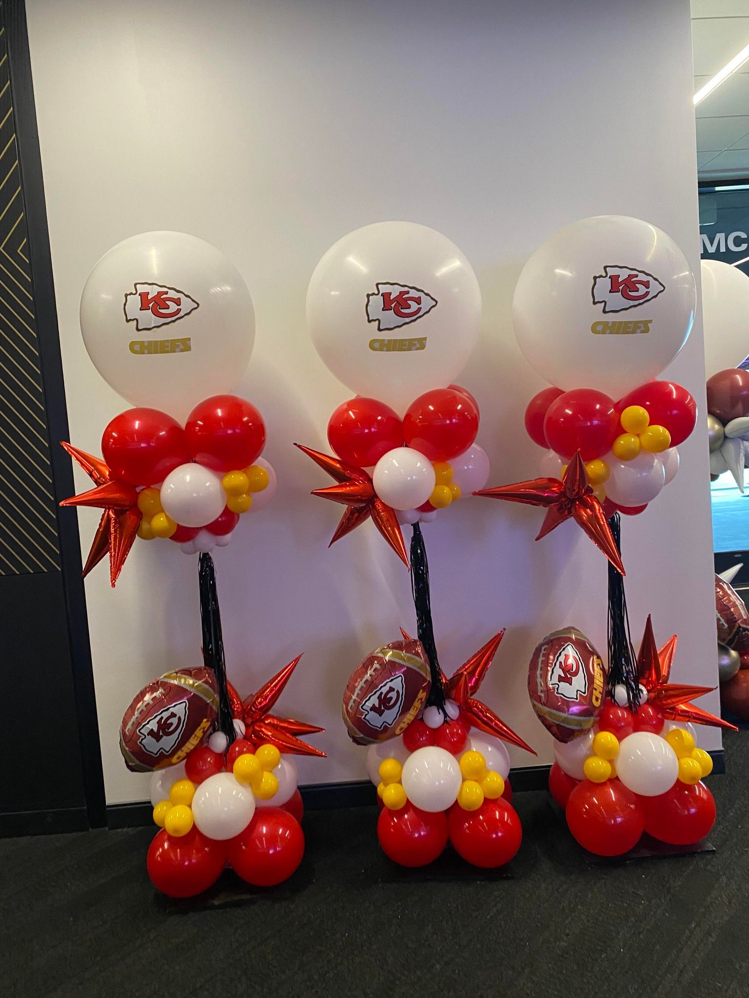 Balloon display with three white logo balloons and red, white, and gold balloon arrangements on stands