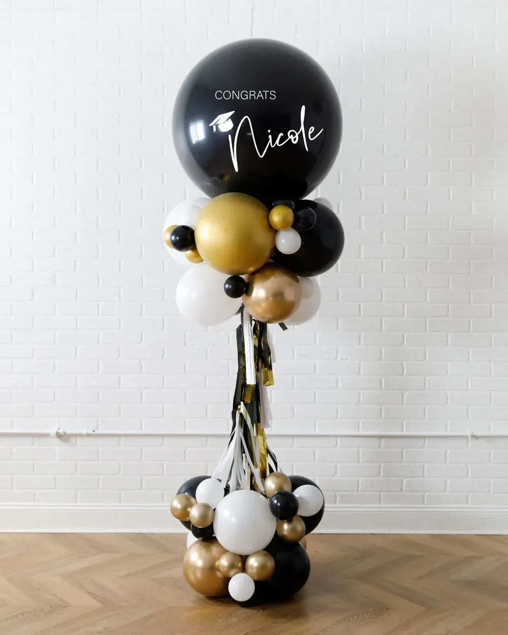 Black, white, and gold balloon column with a personalized black top balloon in a room