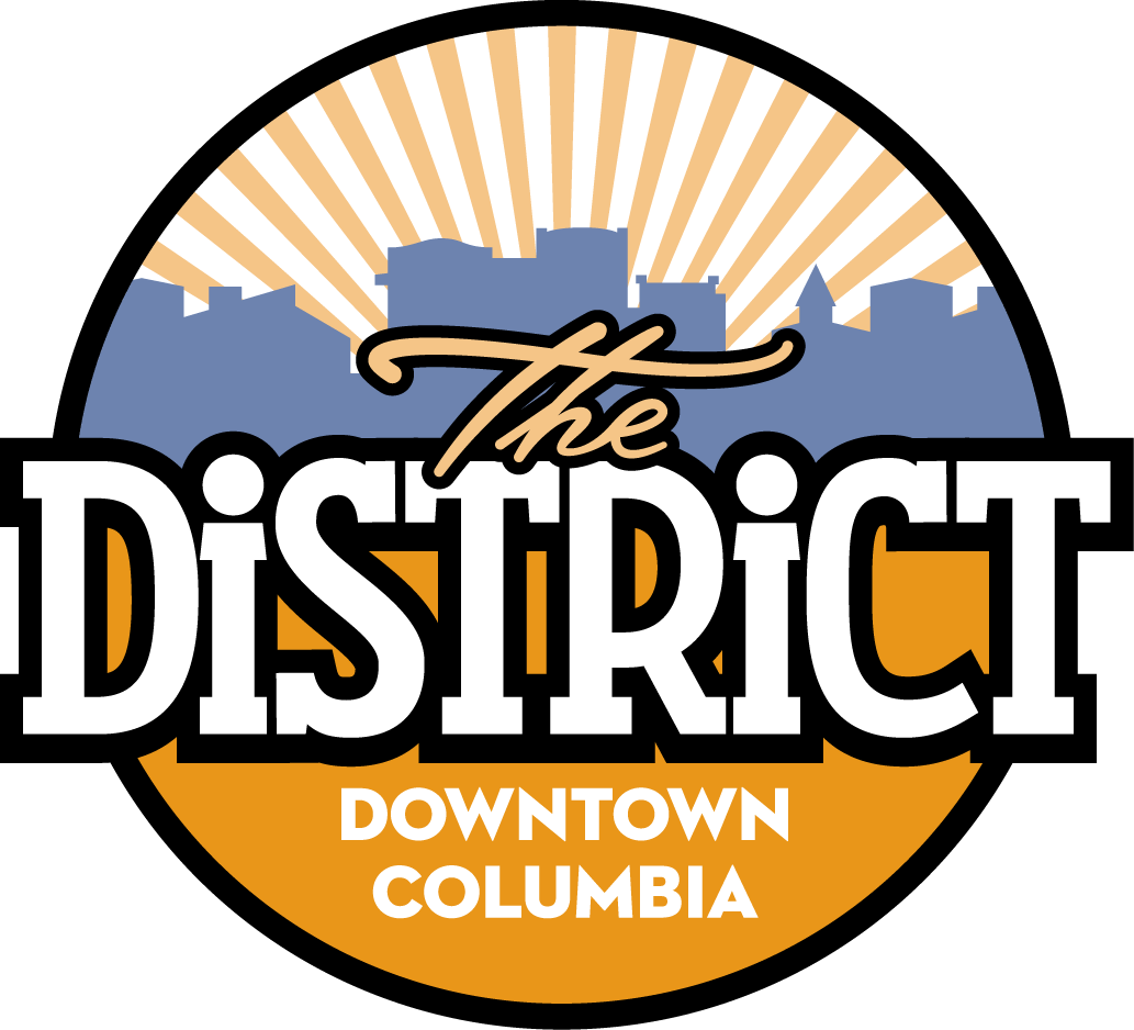 Logo for The District Downtown Columbia with orange sunburst, white lettering, and black border
