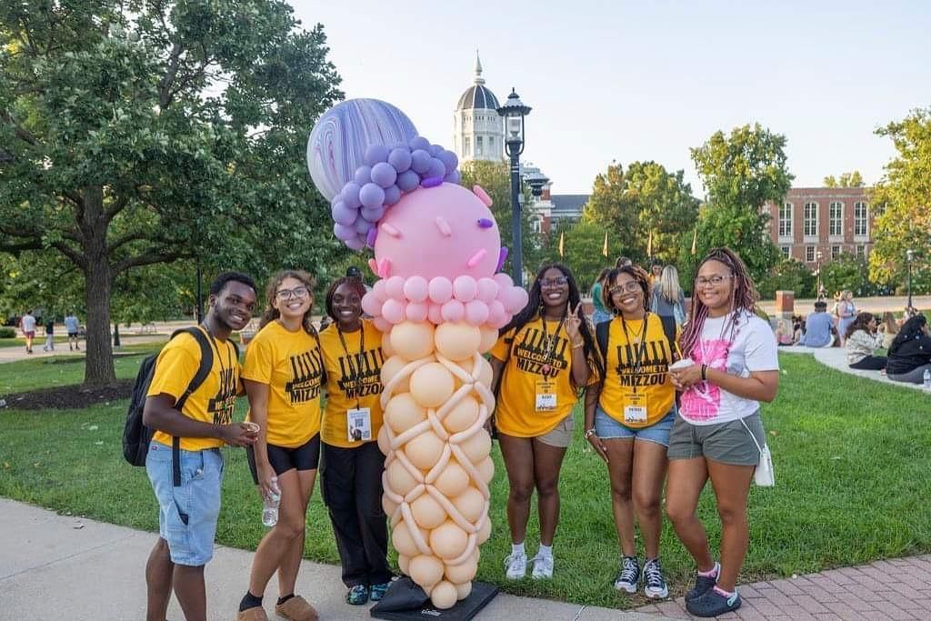 Group of people in yellow shirts posing beside a balloon sculpture in a park.