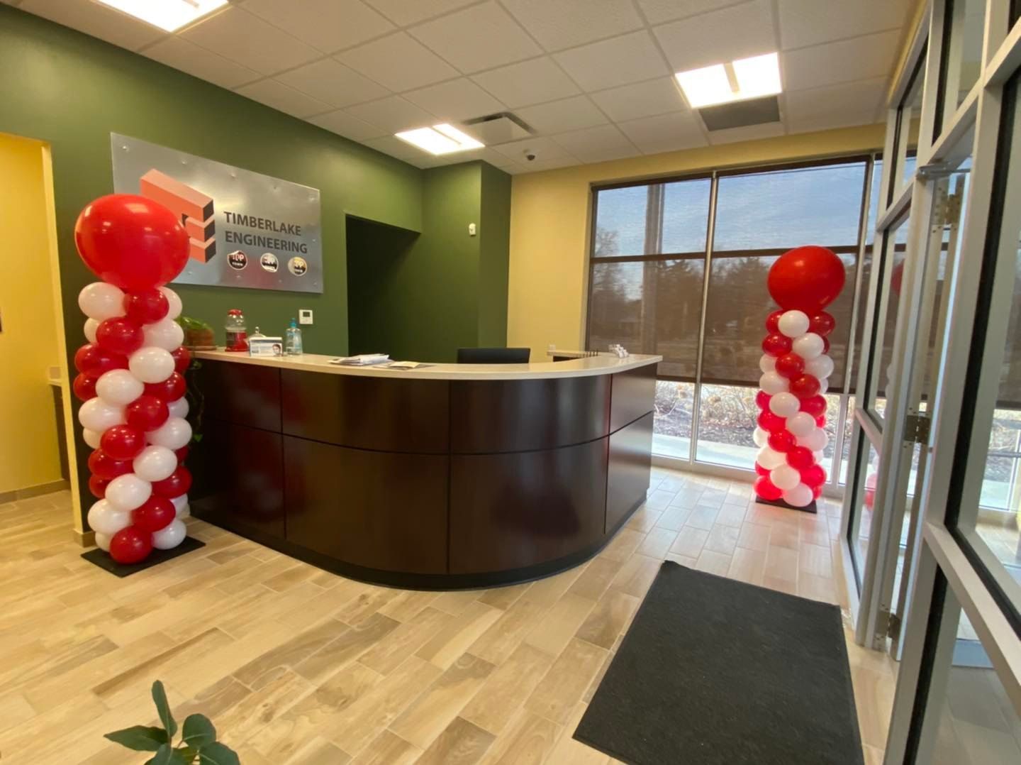 Lobby with a dark wood reception desk, green walls, red-and-white balloon columns, and a snowy view outside.