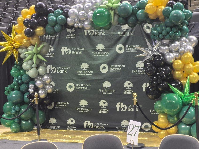 Black and green balloon arch around a step-and-repeat backdrop at a celebratory event photo area